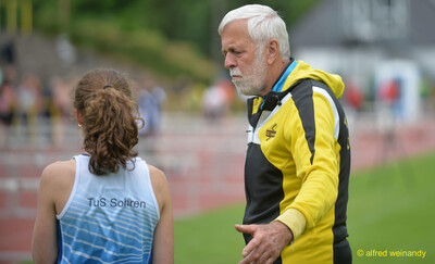 Eine junge Person im Trikot spricht mit einer betreuenden Person in gelber Jacke am Rand der Laufbahn bei der Rheinland-Pfalz-Meisterschaft in Konz.