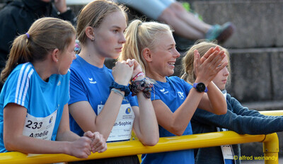 Mehrere Kinder verfolgen an der Bande klatschend den Wettkampf beim Walfried-Heinz-Sportfest der TG Konz im Saar-Mosel-Stadion in Konz.