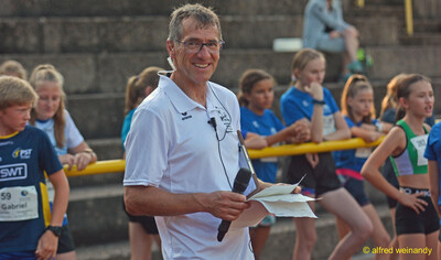 Eine Person mit Mikrofon und Startliste steht vor wartenden Kindern beim Walfried-Heinz-Sportfest der TG Konz im Saar-Mosel-Stadion in Konz.
