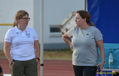 Eine Person im Kampfgericht im Verbandsshirt im Gespräch am Rand der Anlage beim Walfried-Heinz-Sportfest der TG Konz im Saar-Mosel-Stadion in Konz.