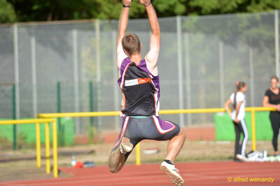 Eine Person springt mit erhobenen Armen hoch in die Luft über der Bahn beim Walfried-Heinz-Sportfest der TG Konz im Saar-Mosel-Stadion in Konz.