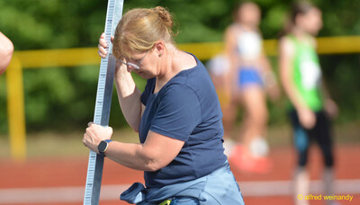 Eine Person im Helferdienst misst mit dem Messstab die Höhe der Hochsprunglatte beim Walfried-Heinz-Sportfest der TG Konz im Saar-Mosel-Stadion in Konz.