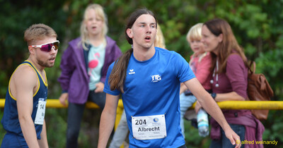 Zwei Aktive in blauen Trikots stehen mit Startnummern zwischen Zuschauenden beim Walfried-Heinz-Sportfest der TG Konz im Saar-Mosel-Stadion in Konz.