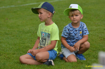 Zwei Kinder sitzen auf dem Rasen und schauen dem Geschehen zu beim Walfried-Heinz-Sportfest der TG Konz im Saar-Mosel-Stadion in Konz.