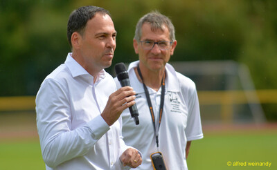 Eine Person spricht ins Mikrofon neben einer Person im Kampfgericht beim Walfried-Heinz-Sportfest der TG Konz im Saar-Mosel-Stadion in Konz.