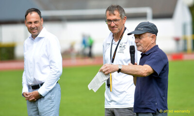 Drei Vereinsverantwortliche stehen zusammen, eine spricht ins Mikrofon, beim Walfried-Heinz-Sportfest der TG Konz im Saar-Mosel-Stadion in Konz.
