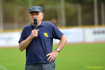 Eine vereinsverantwortliche Person im TG-Konz-Polohemd spricht ins Mikrofon beim Walfried-Heinz-Sportfest der TG Konz im Saar-Mosel-Stadion in Konz.
