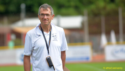Eine Person im Kampfgericht mit Verbandspolohemd und Funkgerät steht auf dem Sportplatz beim Walfried-Heinz-Sportfest der TG Konz im Saar-Mosel-Stadion in Konz.