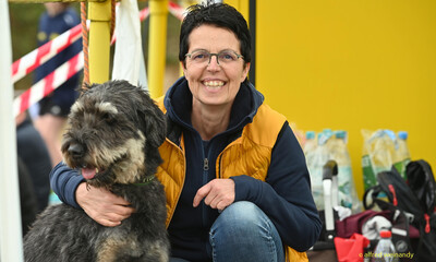 Eine Person kniet lächelnd neben einem Hund am Rand der Wettkampfstätte beim Walfried-Heinz-Sportfest der TG Konz im Saar-Mosel-Stadion in Konz.