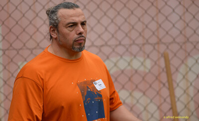 Porträt einer Betreuungsperson im orangefarbenen Shirt vor einem Zaun beim Walfried-Heinz-Sportfest der TG Konz im Saar-Mosel-Stadion in Konz.