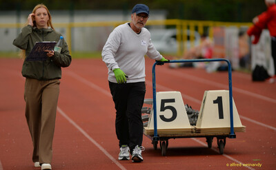Eine Person schiebt einen Wagen mit Bahnnummern-Tafeln über die Laufbahn, eine weitere trägt ein Klemmbrett, beim Walfried-Heinz-Sportfest der TG Konz im Saar-Mosel-Stadion in Konz.