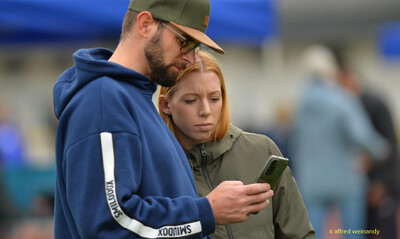 Zwei Zuschauende schauen gemeinsam auf ein Smartphone beim Walfried-Heinz-Sportfest der TG Konz im Saar-Mosel-Stadion in Konz.