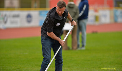 Eine Person beugt sich über eine Metallstange und baut Wettkampfgerät auf dem Rasen auf beim Walfried-Heinz-Sportfest der TG Konz im Saar-Mosel-Stadion in Konz.