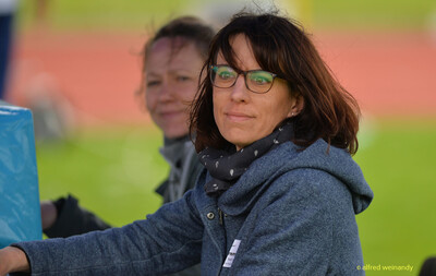 Zwei Personen mit Brille verfolgen das Geschehen, eine lächelt in die Kamera, beim Walfried-Heinz-Sportfest der TG Konz im Saar-Mosel-Stadion in Konz.