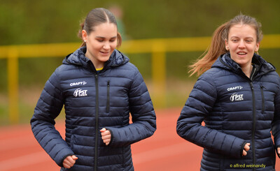 Zwei junge Personen in Vereinsjacken gehen locker über die Laufbahn beim Walfried-Heinz-Sportfest der TG Konz im Saar-Mosel-Stadion in Konz.