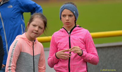 Zwei Kinder in Sportjacken stehen am Rand der Laufbahn beim Walfried-Heinz-Sportfest der TG Konz im Saar-Mosel-Stadion in Konz.