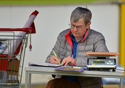 Eine Person im Helferdienst sitzt an einem Tisch mit Waage und notiert Daten beim Walfried-Heinz-Sportfest der TG Konz im Saar-Mosel-Stadion in Konz.