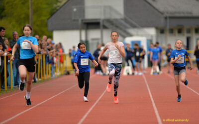 Vier Kinder sprinten mit Startnummern nebeneinander auf der Bahn beim Walfried-Heinz-Sportfest der TG Konz im Saar-Mosel-Stadion in Konz.