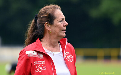Eine betreuende Person in roter Vereinsjacke blickt über das Sportgelände bei der Rheinland-Meisterschaft im Mehrkampf der TG Konz in Konz.