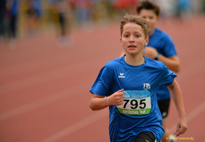 Ein Kind im blauen Trikot läuft konzentriert über die Laufbahn, ein weiteres folgt dahinter, bei der Rheinland-Meisterschaft im Mehrkampf der TG Konz in Konz.