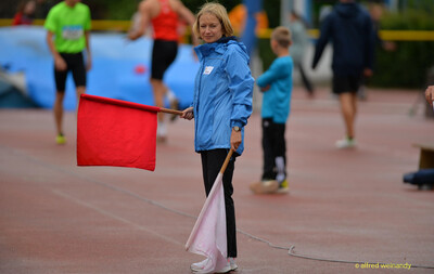 Eine Person im Kampfgericht hält eine rote Signalflagge auf der Laufbahn bei der Rheinland-Meisterschaft im Mehrkampf der TG Konz in Konz.