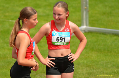 Zwei Jugendliche in roten Trikots stehen auf dem Sportplatz und unterhalten sich bei der Rheinland-Meisterschaft im Mehrkampf der TG Konz in Konz.