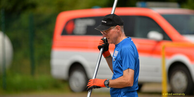Eine Person mit Cap und Handschuhen trägt eine Metallstange über die Anlage bei der Rheinland-Meisterschaft im Mehrkampf der TG Konz in Konz.