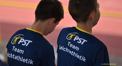 Zwei Jugendliche mit Team-Leichtathletik-Shirts von hinten mit Blick auf die Bahn bei der Rheinland-Meisterschaft im Mehrkampf der TG Konz in Konz.