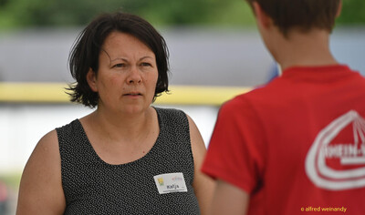 Eine Person mit Namensschild im Gespräch am Rand des Sportgeländes bei der Rheinland-Meisterschaft im Mehrkampf der TG Konz in Konz.