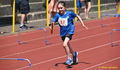 Ein Kind sprintet mit dem Staffelstab in der Hand auf die Kamera zu beim Kinderleichtathletik-Sportfest der TG Konz im Saar-Mosel-Stadion in Konz