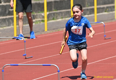 Ein Kind läuft mit dem Staffelholz zwischen den Hürden über die Laufbahn beim Kinderleichtathletik-Sportfest der TG Konz im Saar-Mosel-Stadion in Konz