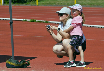 Eine erwachsene Person fotografiert mit einem Kind am Rand der Bahn das Geschehen beim Kinderleichtathletik-Sportfest der TG Konz im Saar-Mosel-Stadion in Konz