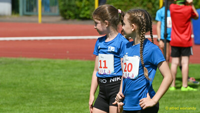Zwei Kinder in blauen Trikots warten mit ihren Startnummern auf dem Rasen beim Kinderleichtathletik-Sportfest der TG Konz im Saar-Mosel-Stadion in Konz