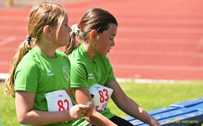 Zwei Kinder sitzen nebeneinander auf einer Bank und ruhen sich aus beim Kinderleichtathletik-Sportfest der TG Konz im Saar-Mosel-Stadion in Konz
