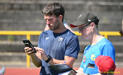 Zwei Helfende schauen gemeinsam auf ein Handy und notieren Ergebnisse beim Kinderleichtathletik-Sportfest der TG Konz im Saar-Mosel-Stadion in Konz