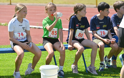 Kinder sitzen auf einer Bank und trinken in der Pause beim Kinderleichtathletik-Sportfest der TG Konz im Saar-Mosel-Stadion in Konz